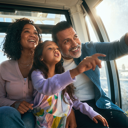Father and daughter pointing out of gondola ride while mother looks on smiling