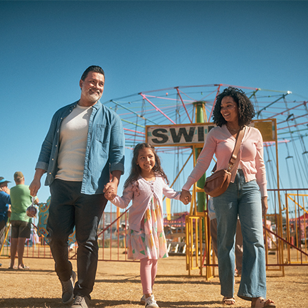 father and mother holding hand of daughter with swing ride behind them