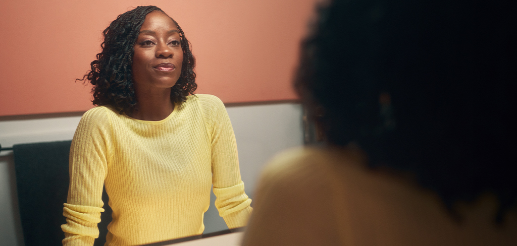 Mujer luciendo un suéter amarillo mirándose en el espejo.