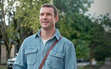 One woman stands while two are sitting in a conference room with laptops on the desk